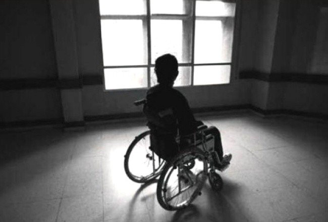 Imagen en blanco y negro de una mujer en silla de ruedas a contra luz en una habitación vacía